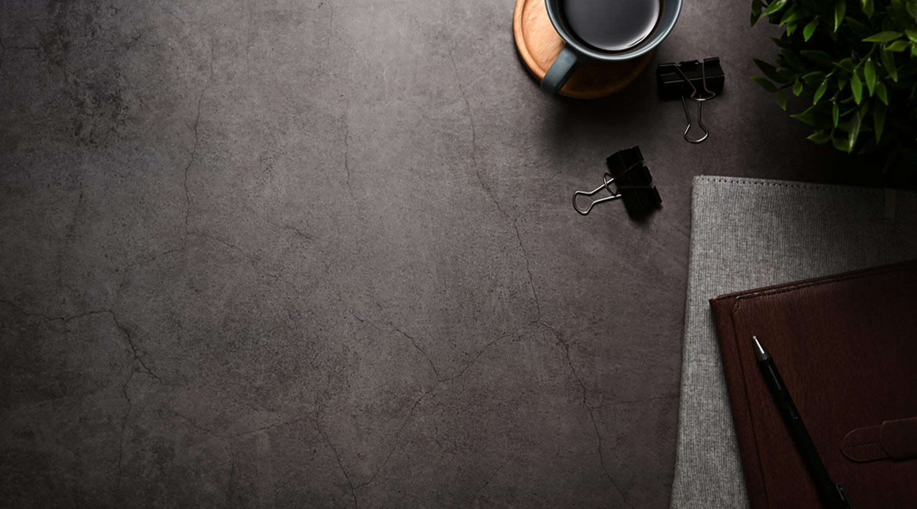 Dark gray textured desk with office supplies including a mug, clips, and a notebook.